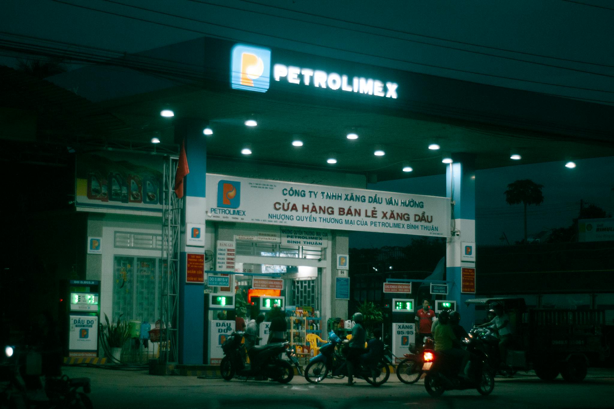 Motorcycles at a Petrolimex gas station in Vietnam at night with vibrant lighting.