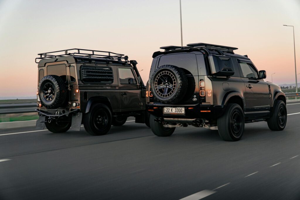 Two Land Rover Defenders driving on a highway in Erbil at sunset, showcasing urban adventure.