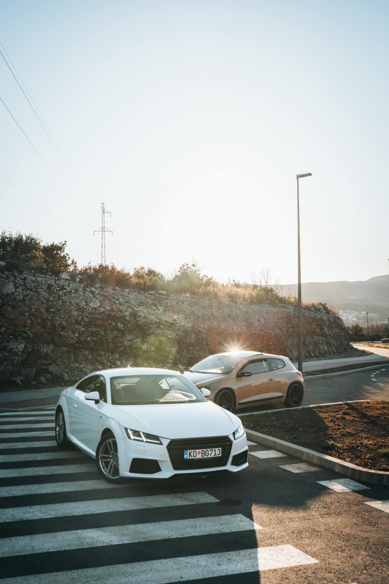 Two sleek cars on a sunny road in Tivat, Montenegro, showcasing modern automotive design.